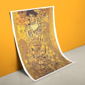 Könnte beinhalten: Kunstdruck von Gustav Klimts "Porträt der Adele Bloch-Bauer I". Der Druck zeigt eine Frau in einem goldenen Kleid mit komplizierten Mustern und Details. Das Kunstwerk lehnt an einer gelben Wand.
