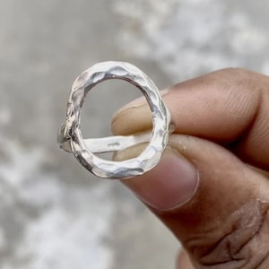 Könnte beinhalten: Ein silberner Ring mit einem gehämmerten, kreisförmigen Design. Der Ring ist offen und hat eine glatte, polierte Oberfläche.