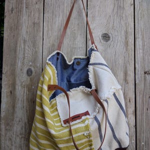 May include: A patchwork tote bag with a mix of fabrics. The bag incorporates yellow and white striped material, denim, and cream fabric with blue stripes. It has brown leather handles and a brown leather base.