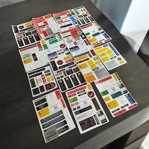 以下が含まれることがあります： 赤、黄、青のアクセントが付いた白黒の警告ステッカーのコレクション。ステッカーには、電気の危険に関する警告、安全に関する指示、注意喚起のメッセージなど、さまざまな記号とテキストが記載されています。