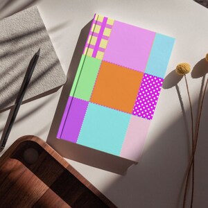 以下が含まれることがあります： パッチワークデザインのカラフルなジャーナル。表紙にはピンク、オレンジ、グリーン、パープル、ブルーの正方形があり、水玉模様やチェック柄のものもあります。ジャーナルは、鉛筆と木製のトレイと一緒に白い表面に置かれています。