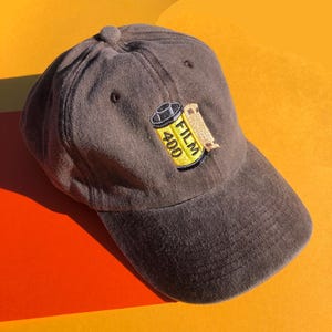 May include: A brown baseball cap with an embroidered yellow film canister with the text "FILM 400" on it.