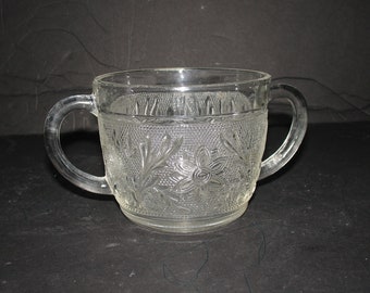 May include: A clear glass sugar bowl with two handles and a floral pattern.