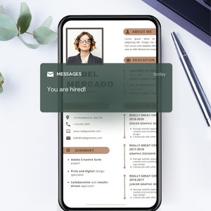 Puede incluir: Un smartphone muestra un currículum con el nombre de Bel Mercado, diseñadora gráfica. Un bocadillo de mensaje dice "¡Estás contratado!". El teléfono está sobre una superficie blanca con un teclado y un bolígrafo.