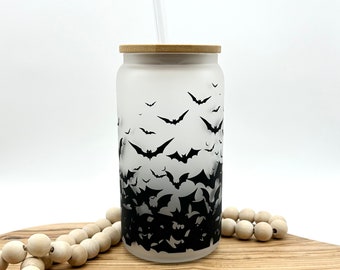 May include: A frosted glass tumbler featuring a black bat pattern that transitions from sparse at the top to dense at the bottom. The cup includes a light-colored bamboo lid and a clear glass straw, creating a functional beverage container.