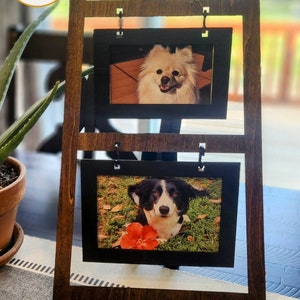 May include: A wooden picture frame stand with two black picture frames. The top frame shows a white fluffy dog, and the bottom frame shows a black and white dog with a red flower.