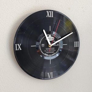 May include: Black vinyl record clock with white Roman numerals at the 12, 3, 6, and 9 o'clock positions. The clock hands are white, with a red second hand. The center label reads "DECCA" and "NOCTURNES".