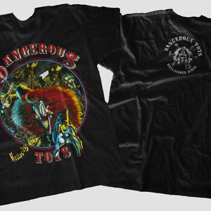 May include: Black t-shirt with a colourful graphic on the front featuring a wolf-like creature with the text "DANGEROUS TOYS" and "Hellacious Acres". The back of the shirt has a smaller circular design with the same text.