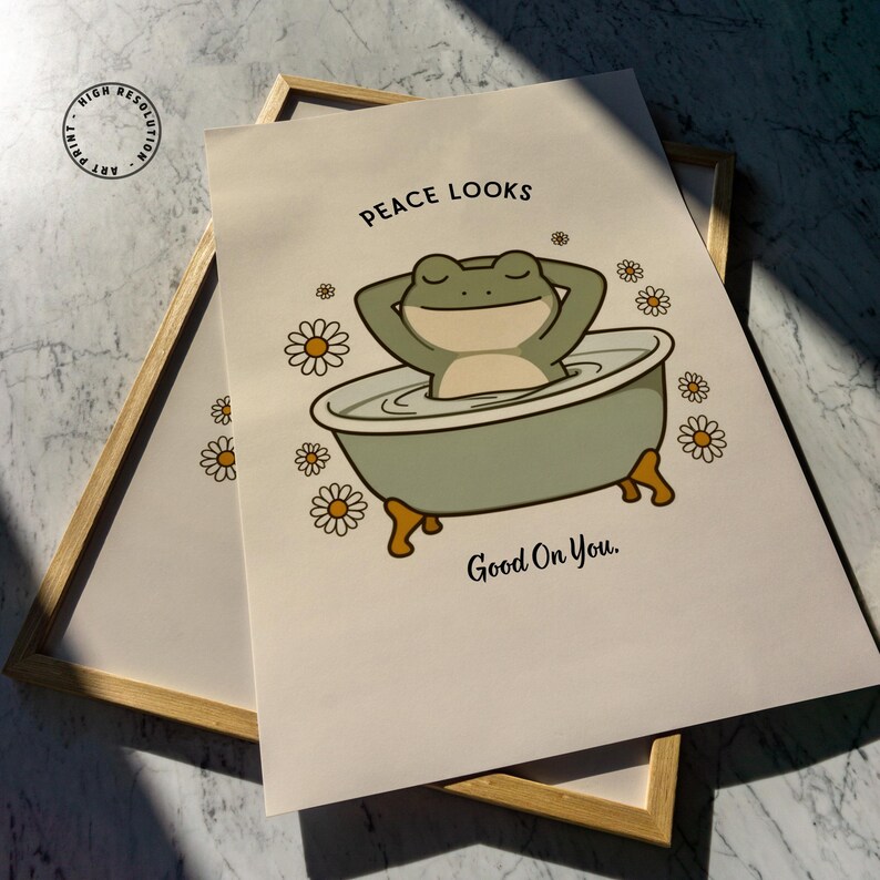 Puede incluir: Una impresi&oacute;n art&iacute;stica enmarcada con una rana de dibujos animados en una ba&ntilde;era. La rana es verde y beige, con los brazos detr&aacute;s de la cabeza. La impresi&oacute;n incluye el texto "Peace Looks Good On You" e ilustraciones de margaritas.