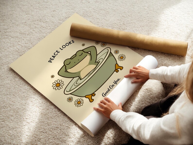 Puede incluir: Un p&oacute;ster beige con una rana de dibujos animados relaj&aacute;ndose en una ba&ntilde;era, rodeada de margaritas. El texto "Peace Looks Good On You" est&aacute; impreso en el p&oacute;ster. Tambi&eacute;n se ven un p&oacute;ster enrollado y un tubo marr&oacute;n.