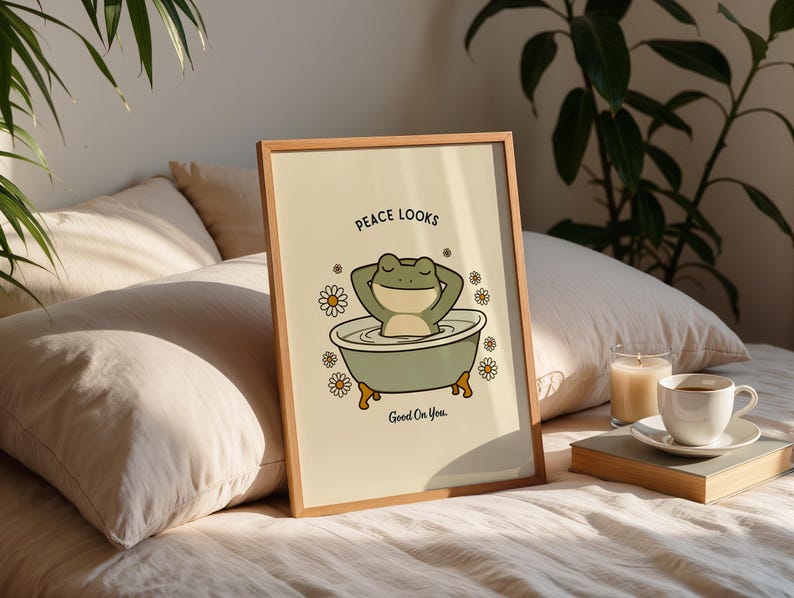 Puede incluir: Un cuadro enmarcado con una ilustraci&oacute;n de una rana de dibujos animados en una ba&ntilde;era. La rana es verde y relajada, y la ba&ntilde;era es verde claro con patas doradas. El texto "Peace Looks Good On You" est&aacute; incluido. El marco es de madera.