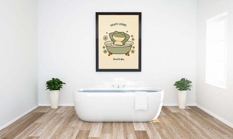 Puede incluir: Un cuadro enmarcado con un dibujo de una rana de dibujos animados relaj&aacute;ndose en una ba&ntilde;era, con el texto "Peace Looks Good On You". La obra de arte est&aacute; sobre un fondo crema, rodeada de margaritas. El ba&ntilde;o tiene una ba&ntilde;era blanca y plantas.