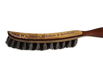 May include: A wooden brush with a brown handle and black bristles. The handle has the text "The 2 W's. Hatters. Newcastle & Gateshead."