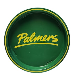 Può includere: Un coperchio rotondo in plastica verde scuro con la parola Palmers stampata in un carattere corsivo giallo al centro. Il coperchio presenta un sottile bordo circolare giallo vicino al bordo esterno e piccole rientranze rettangolari sul bordo interno.