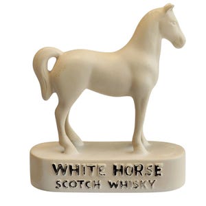 Può includere: Statuetta di cavallo color crema su una base rettangolare. La base presenta la scritta "WHITE HORSE SCOTCH WHISKY" in lettere nere. Il cavallo è scolpito in una posa realistica.