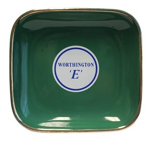 Può includere: Un piattino quadrato in ceramica verde scuro con angoli arrotondati e un bordo metallico color oro. Al centro, un adesivo circolare bianco presenta un bordo blu con il testo "WORTHINGTON" e la lettera "E" stampati in blu.