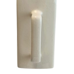 May include: Cream-coloured ceramic mug with a rectangular body and a curved handle. The mug has a crackle glaze finish, adding a textured appearance. The handle is smooth and rounded, contrasting with the textured body.