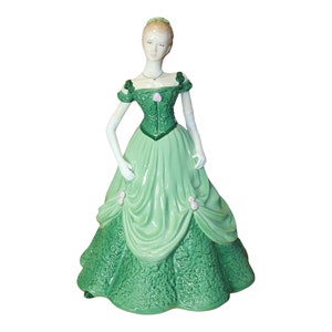 Könnte beinhalten: Eine Porzellanfigur einer Frau in einem grünen Kleid mit Blumenmuster. Sie trägt eine Perlenkette und ihre Haare sind nach hinten gebunden.