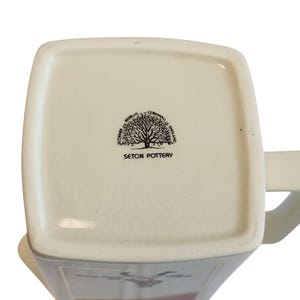 May include: Cream ceramic mug with a square base and a handle. The base features a black tree logo and the words "SETON POTTERY". The mug has a rectangular shape and a slightly glossy finish. Made in England.