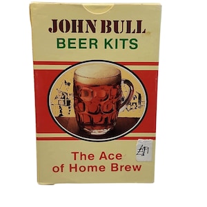 Può includere: Una scatola rettangolare in cartone per kit per birra John Bull. La confezione color crema presenta strisce orizzontali rosse e una grafica circolare centrale che mostra un boccale di vetro con fossette pieno di birra. Il testo recita John Bull Beer Kits e The Ace of Home Brew.