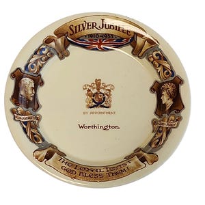 Può includere: Un piatto commemorativo in ceramica color crema con il testo Silver Jubilee 1910-1935, i ritratti di Re Giorgio V e della Regina Maria, uno stemma reale, il testo By Appointment Worthington e la frase The Loyal Toast God Bless Them.