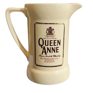 Può includere: Una brocca per l'acqua in ceramica color crema con un'etichetta marrone scuro che riporta la scritta Queen Anne Rare Scotch Whisky, Hill Thomson & Co. Ltd. Edinburgh Established 1793, uno stemma e un manico curvo sul lato.