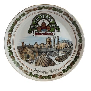 Può includere: Un piatto commemorativo rotondo in ceramica bianca con un'illustrazione colorata di un birrificio con pile di botti di legno. Il testo recita 150 YEARS OF 1834 1984 Marston's Brewing Excellence. Il bordo è decorato con un motivo di luppolo e grano.