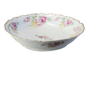 Puede incluir: Un tazón grande de porcelana blanca con un borde festoneado y un diseño floral. El tazón está decorado con rosas rosas, amarillas y verdes.