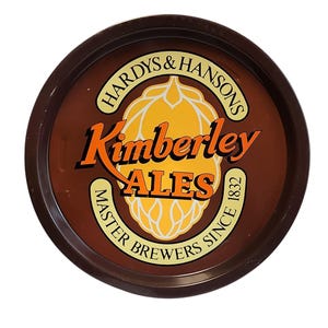 Può includere: Un vassoio da portata rotondo in metallo marrone con il logo Hardys & Hansons Kimberley Ales al centro. Il design include una grafica di luppolo giallo, il testo Kimberley ALES e le parole MASTER BREWERS SINCE 1832 in un bordo circolare.