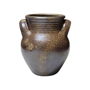May include: A speckled brown ceramic vase with two handles. The vase has a wide, textured rim and a rounded body that tapers towards the base. The color gradient transitions from dark brown to a lighter brown.