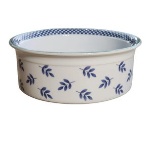 May include: A round, cream-coloured ceramic bowl featuring a blue leaf pattern and a blue and white chequered rim. The bowl has a light green trim around the top edge. The design is simple and elegant.