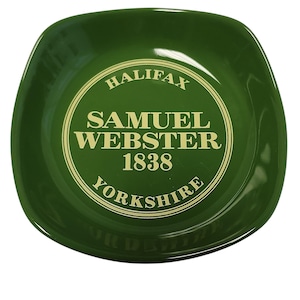 Può includere: Un piatto quadrato in ceramica verde scuro con angoli arrotondati. Il centro presenta un emblema circolare color oro con il testo "HALIFAX", "SAMUEL WEBSTER", "1838" e "YORKSHIRE" stampato in un carattere chiaro e senza grazie.