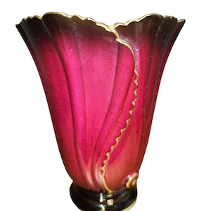 Puede incluir: Un jarrón de cerámica rojo y negro con ribete dorado. El jarrón tiene un diseño único y ondulado y una abertura ancha.