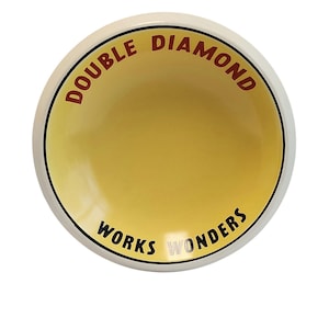 Può includere: Una ciotola rotonda in ceramica con interno giallo ed esterno bianco. Il bordo interno presenta il testo DOUBLE DIAMOND in lettere rosse nella parte superiore e il testo WORKS WONDERS in lettere nere nella parte inferiore, separati da una sottile linea nera.