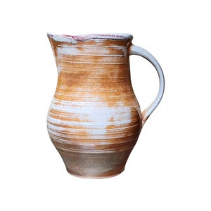 May include: A handmade ceramic pitcher with a white handle and a wide, open spout. The pitcher has a brown and white striped design, with a light brown base and a red rim. This rustic pitcher is perfect for serving beverages.