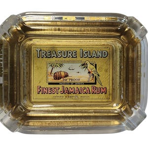 Può includere: Un posacenere rettangolare in vetro con interno dorato e un'etichetta centrale per Treasure Island Finest Jamaica Rum. L'etichetta mostra un barile, una palma, un pappagallo e il testo 70 PROOF, PRODUCE OF JAMAICA, HAWORTH & AIREY LTD.