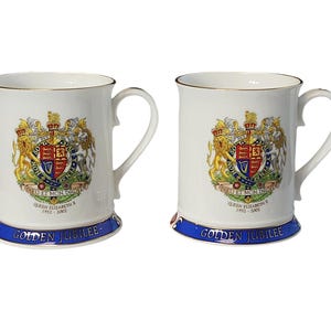 May include: Two white ceramic mugs with blue and gold trim. Each mug features a colorful coat of arms with a lion, unicorn, and a shield with the text "DIEU ET MON DROIT". The text "QUEEN ELIZABETH II 1952 - 2002" and "GOLDEN JUBILEE" are printed on the bottom of each mug.