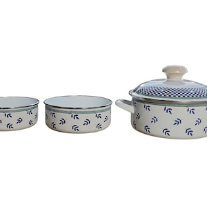 May include: A collection of three enamelware cooking pots and bowls. The set includes two bowls and a pot with a lid. The pots and bowls are white with a blue leaf pattern and a blue and white checkered pattern on the lid.