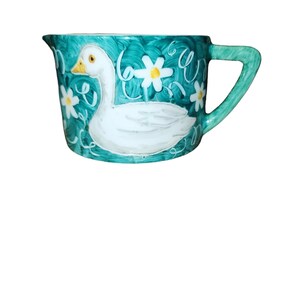 May include: A teal blue ceramic pitcher with a white goose design and white daisy accents.