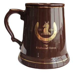 Può includere: Un boccale da birra in ceramica marrone con bordo e manico dorati. Il boccale presenta un design a ferro di cavallo dorato con un cavallo e il testo "The Whitbread Shires" e "EST 1742".