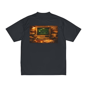 May include: A dark charcoal gray short-sleeve t-shirt featuring a graphic print of a vintage computer monitor displaying a green error message box with the text 'The hallucinations are real' on a desk with stacks of papers and a lamp.