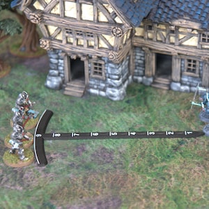 May include: A miniature tabletop wargaming scene with a small stone building in the center. A group of silver-colored miniature figures stand facing a group of blue-colored miniature figures. A ruler is placed between the two groups of figures.