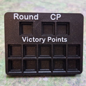 May include: Black plastic game tracker with white text that reads "Round", "CP", and "Victory Points". The tracker has spaces for keeping score.