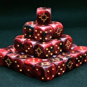 Könnte beinhalten: Eine Pyramide aus rot-schwarzen Würfeln mit goldenen Markierungen. Jeder Würfel hat goldene Augen und ein goldenes Emblem auf der Oberseite. Die Würfel sind auf einer dunkelgrünen Oberfläche angeordnet.