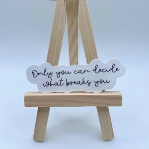 May include: White sticker with a cloud shape and the text "Only you can decide what breaks you" in black script. The sticker is on a small wooden easel.