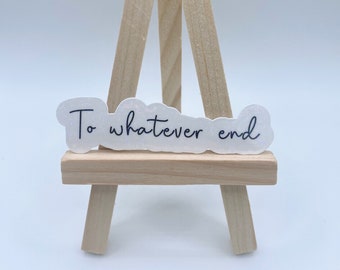 May include: A white sticker with the text "To whatever end" on a small wooden easel.