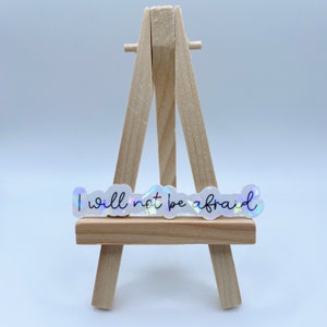 May include: A white sticker with iridescent glitter accents on a wooden easel. The sticker says "I will not be afraid" in a handwritten font.