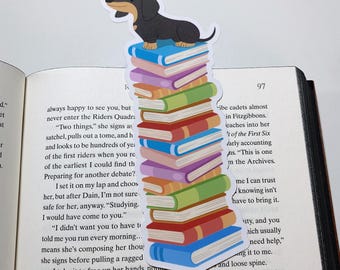 Puede incluir: Un marcapáginas de dachshund con un dachshund negro y marrón sentado encima de una pila de libros coloridos. El marcapáginas está en una página de un libro con texto que dice "siempre feliz de verte, pero nunca entres en los Riders Quadra. "Dos cosas," ella firma mientras saca su mochila, saca un libro y h y parece que hay cientos de años de la primera generación de jinetes cuando estás entre los más antiguos que pude encontrar. Preparando para otro debate? Lo pongo en mi regazo y elijo ella, pero después de Dain, no estoy seguro de que sea seguro para ella, de todos modos. "Estudiando. Yo habría venido a ti." "No quería que tuvieras que decirme que corres todas las mañanas... eso significa que está componiendo sus pensamientos, ella firma antes de sacar un trozo de tela desgarrado, lo tomo para liberarle las manos, no "Estoy tratando de traducir esto para una tarea, y estoy luchando con un par de oraciones. Está en Old Lucerish, y por lo que recuerdo, es uno de los idiomas muertos que puedes leer." Sus mejillas se sonrojan de rosa mientras mira hacia atrás"