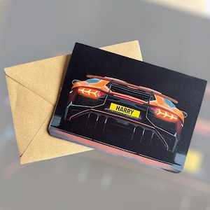 May include: Greeting card featuring an orange sports car illustration with the license plate reading "HARRY" against a black background. The card is paired with a brown envelope.
