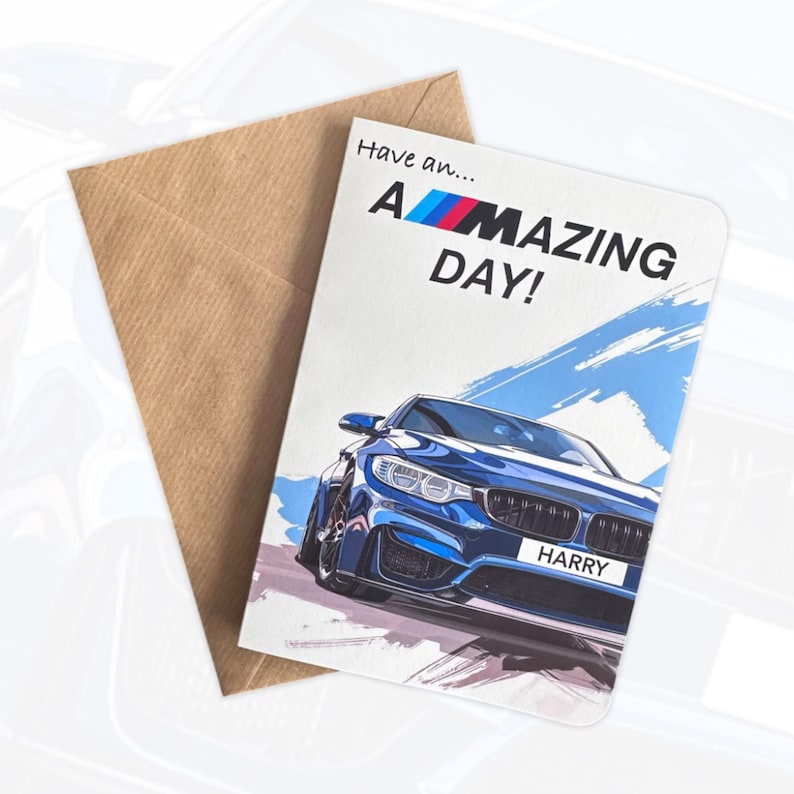 May include: A white greeting card with a brown envelope featuring a blue sports car illustration and the text Have an... A-MAZING DAY! The car has a license plate that reads HARRY and the letter M in the text is stylized with blue, purple, and red stripes.
